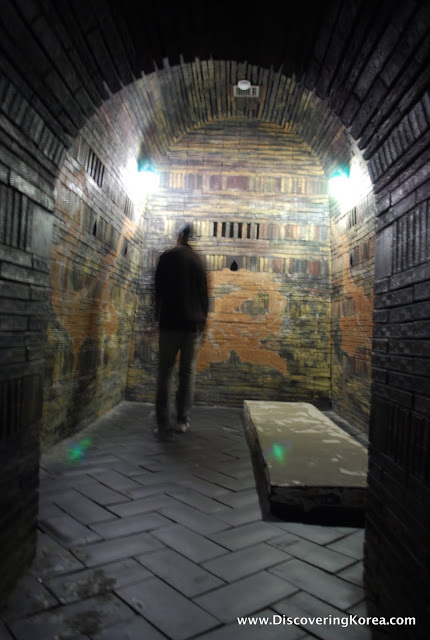 The blurry outline of a man inside one of the Songsanri Tombs. The interior features ancient bricks set in a barrel vault with a raised stone platform for burial.