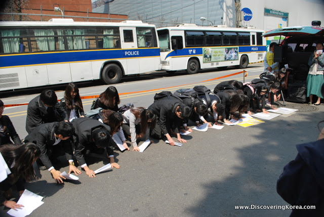 Korean school children kneeling on their hands and knees paying customary respect to the elder former comfort women.