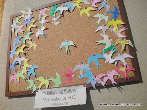 Paper birds made by Japanese school children and given to former Korean comfort women as a show of solidarity. They paper birds are pinned to a cork boarded.