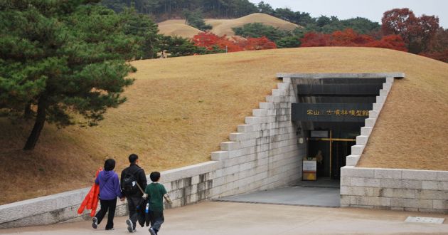 A small family of Korean walk into an earthen mound that contains the entranc to one of the Songsanri Tombs of Gongju Korea.