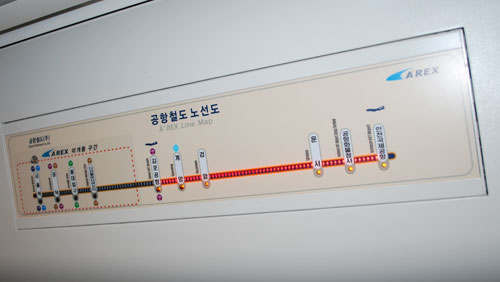 The airport train route shown on a sign inside of a subway car.