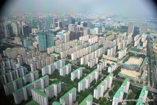 An artist's view of Yeouido island from the air, with neat rows of tall buildings and skyscrapers, green space and the river in the background.