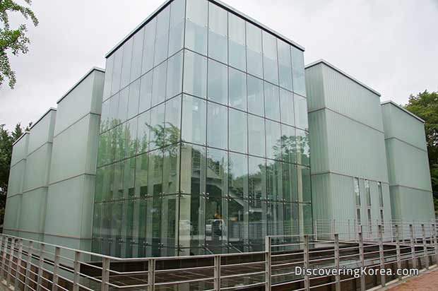 Glass buildings seen from the outside, with metal railings around them, and a cloudy sky.