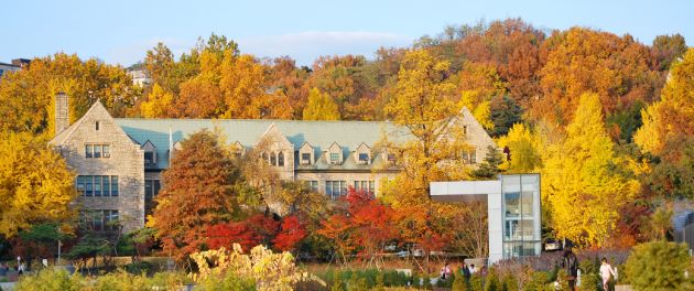 A large stone house with light green roof nestled amongst trees with their yellow, red, and orange autumnal leaves.