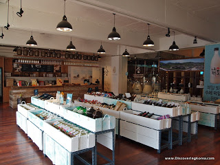 Shop display of bottles of rice beer, in white rows, with a cafe counter behind and lights hanging from the ceiling. The floor is hardwood.