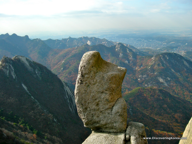 A rock formation in the foreground, with mountains overlooking Seoul in the background.