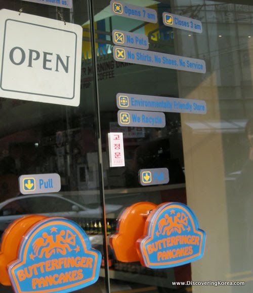 Glass front doors of a cafe in Seoul. The blue and orange handles say Butterfinger Pancakes, and there is a black and white sign, and various text signs in gray and blue.