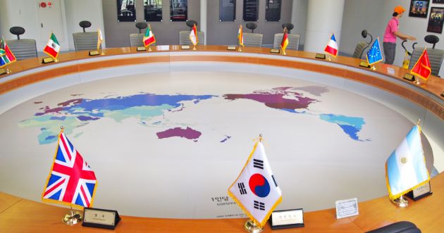 A circular meeting table in light wood, with a map of the world in the center. Flags from each nation around the table at Cheongwadae Sarangchae.