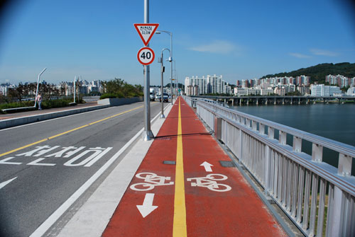 Looking over the bridge towards the city, the river on the right of the frame, a cycle lane in the center of the frame and road on the left.