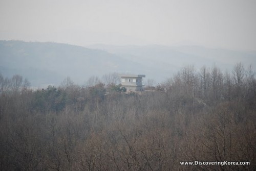 A solitary house sits in scrubby bushland with mountains in the background. DMZ nature preserve.