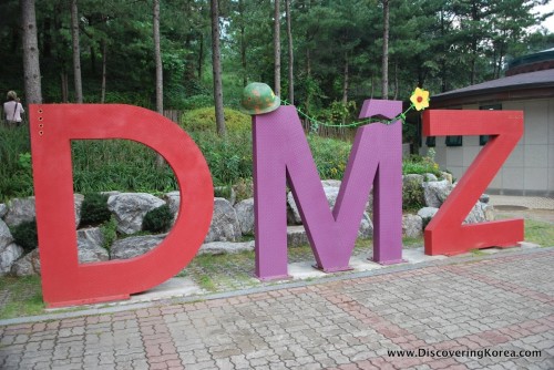 The letters DMZ in red and purple in front of trees.