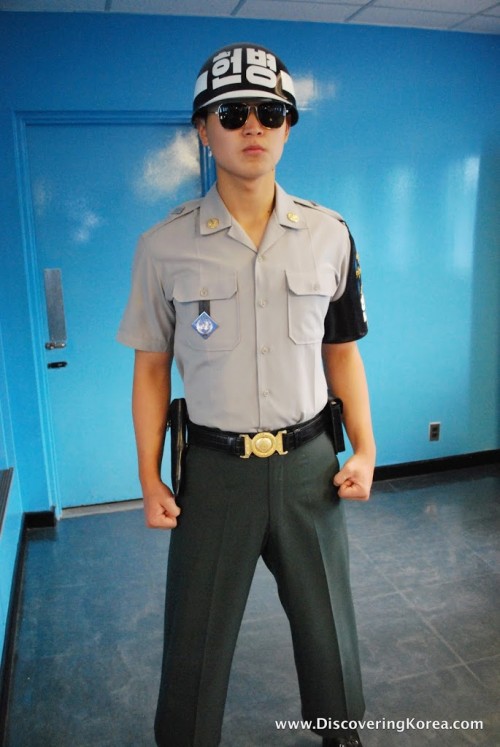 A soldier in the DMZ stands with his fists clenched in front of a blue wall.