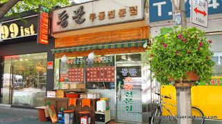 Shop front of a restaurant in Yongsang, with tables outside, and an ornamental bush to the right of the frame.