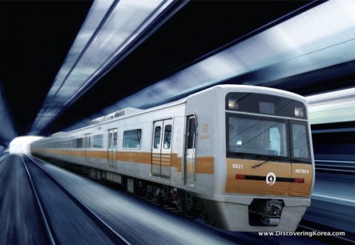 Close up of a metro train, white with a yellow stripe, speeding through a metro tunnel in Seoul.