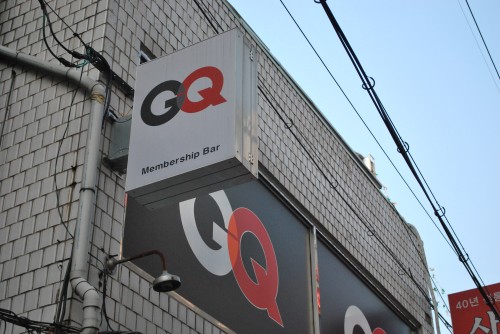 A white tiled exterior of a building showing a close up of a sign to a membership bar, in black and red.