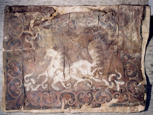 A faded painting on wood, of a white horse, and an ornate black and red border.