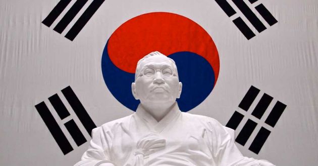 White statue of a Korean man, on a white background, with a red and blue yin-yang symbol behind and four black symbols consisting of parallel lines.