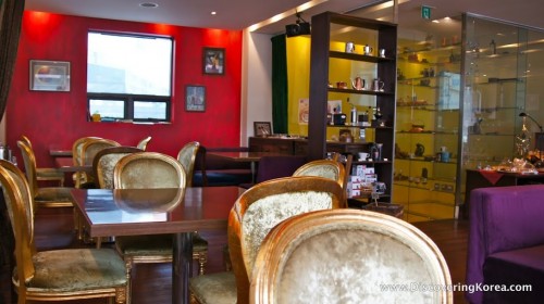 Chairs and tables arranged in a cafe, with a red wall in the background and glass display cabinets to the right of the frame.