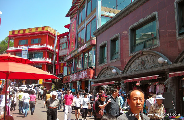 Street scene in Incheon, with red buildings in the background and pedestrians.