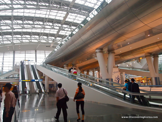 Incheon airport building, showing an escalator, light coming in through glass ceiling and commuters.