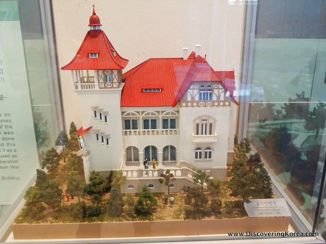 Scale model of a white building with a red roof inside a glass case.