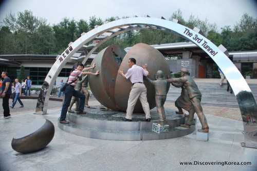 The 3rd infiltration tunnel picturing men pushing a bronze statue of a sphere cut in half.