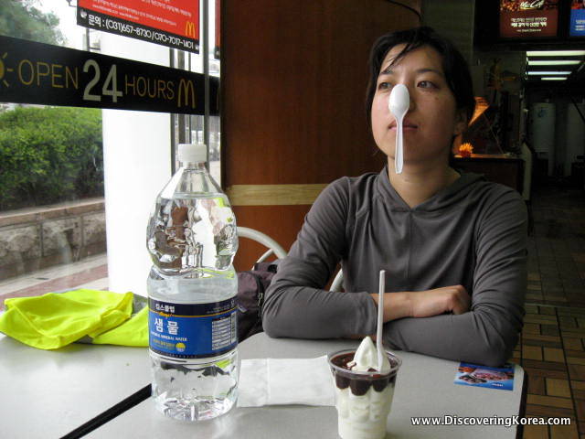 A woman in a cafe, with a plastic water bottle on the table in front of her, and an ice cream sundae.