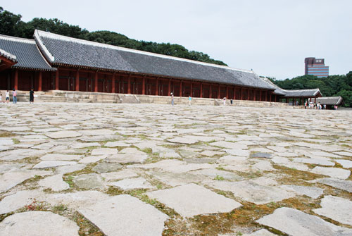 Paved area outside the Jongmyo Royal Shrine, with the building in the background, red pillars and dark roof.