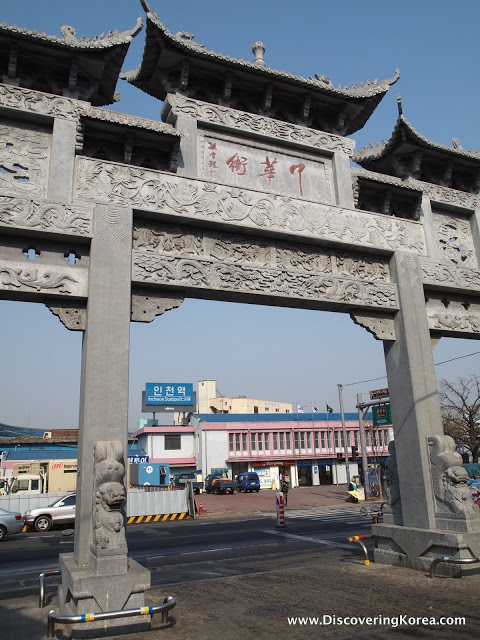 Close up of Junghwamun Pailou gate showing carved stonework and buildings in the background.