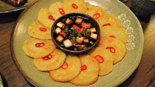 A Korean dish on a light green plate, of pancakes making a circle around a center dish of tofu in a dark broth.