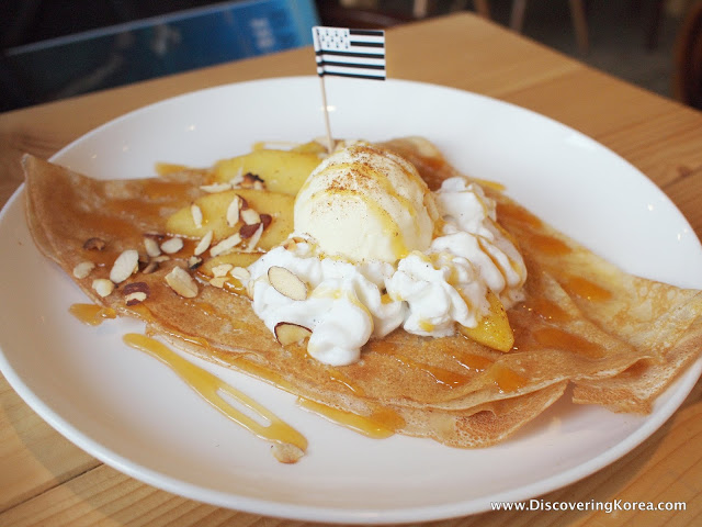 Close up of a thin pancake with cream, ice cream, almond slices and caramel sauce, on a white plate with a small flag, on a wooden table.