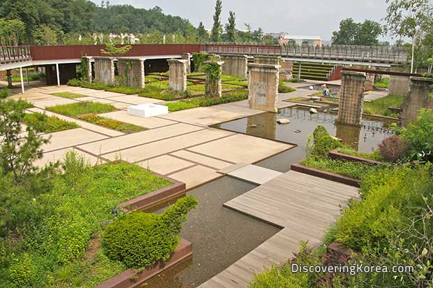 Geometric pathways through a water feature, with a bridge, various patches of vegetation amongst the large stone slabs.