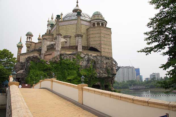 View over a bridge, with the river to the right of the frame, an impressive stone building with dome roof and pillars, built on a cliff face. In the background is Seoul city.