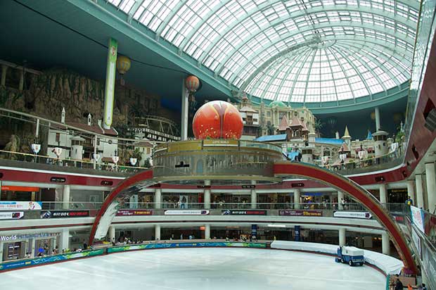 A glass dome ceiling above a shopping arcade, with a large structure in the center, with an arched frame above it.