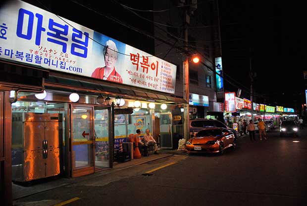 Night time view of Ma Bok-lim restaurant, a glass shop front with a brightly lit sign above it.