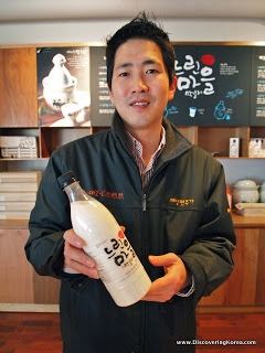 Man holding a bottle of Makgeolli rice beer, in a shop.