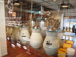 Rice beer being brewed in light stone colored ceramic pots, with metal tops behind a glass shop front.