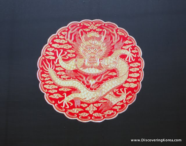 A red, circular motif in red and gold depicting a dragon on a black background.