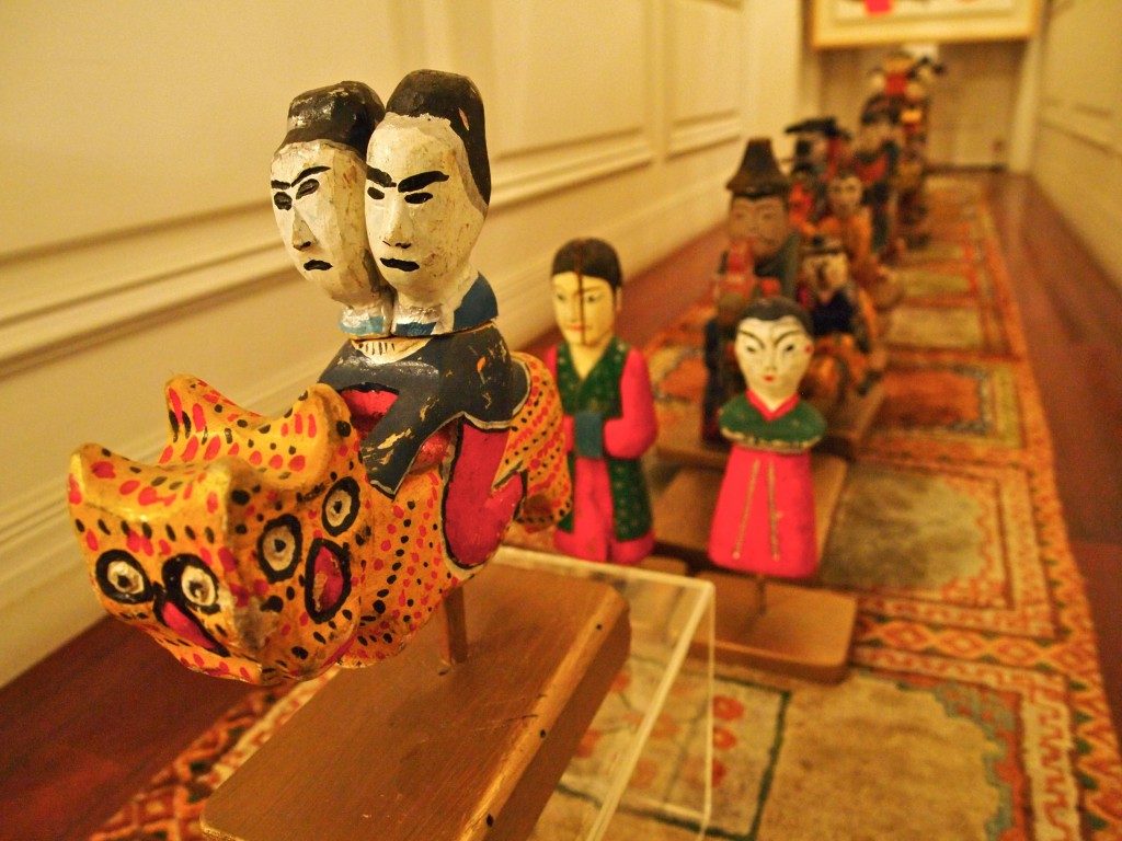 Wooden carvings, in a long line, depicting people riding on mythical animals, people walking, dressed in traditional Korean clothes, on a patterned carpet.