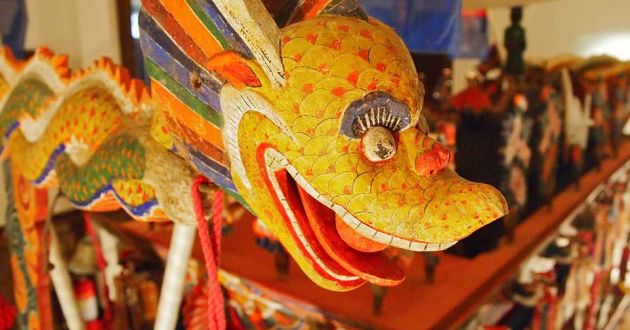 Close up of a carved wooden dragon, with yellow and red scales, multicolored body and wings at Musee Shuim.