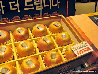 A box with partitions, each section containing an apple, with a label around it. In the foreground is a printed label showing the price.