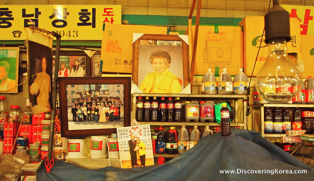 A shop, with yellow walls and pictures, with shelves stocked with various condiments in bottles.