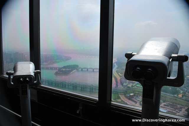 View through the glass windows of the observatory at 63 building Seoul. Two fixed binocular and the river and city in the background.
