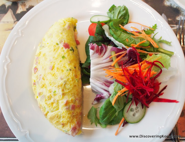 A white plate with an omelette on the left, and a mixed salad on the right.