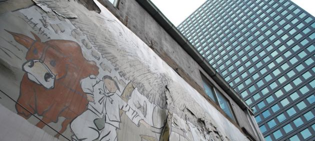 To the left of the frame is a painted concrete wall, showing a man with a cow, to the right of the frame is a glass high rise modern building in Seoul.