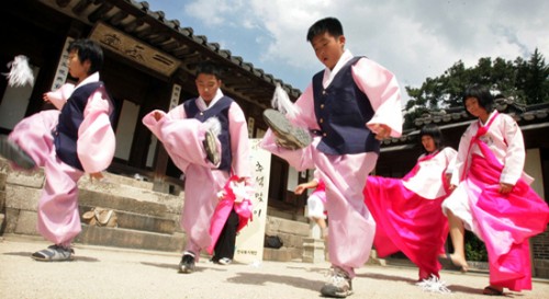 Traditional Korean dancers, in pink with black waistcoats perform a traditional Seollal dance outside a building.