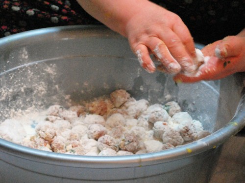 Two hands to the top right of the frame form meatballs in a metal bowl. The metal bowl contains meatballs with a light dusting of flour, for a traditional Seollal feast.