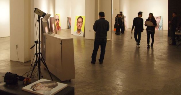 People walking around the Seoul Art Gallery, with pictures resting against walls, and an open space with a spotlight in the center.