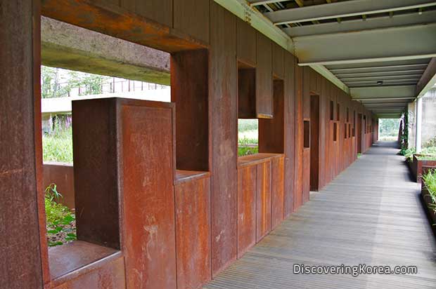 A covered walkway at Seoul Lake Park, with deep red, rust-colored side with geometric openings as windows.