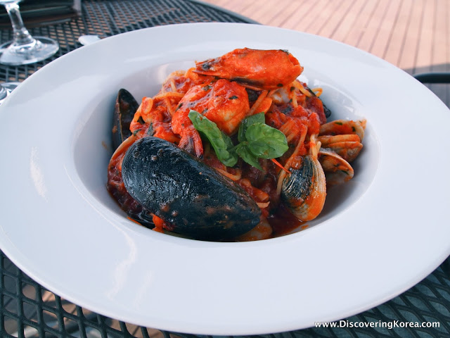 A white bowl with seafood pasta, mussels and shrimp, on a metal table.